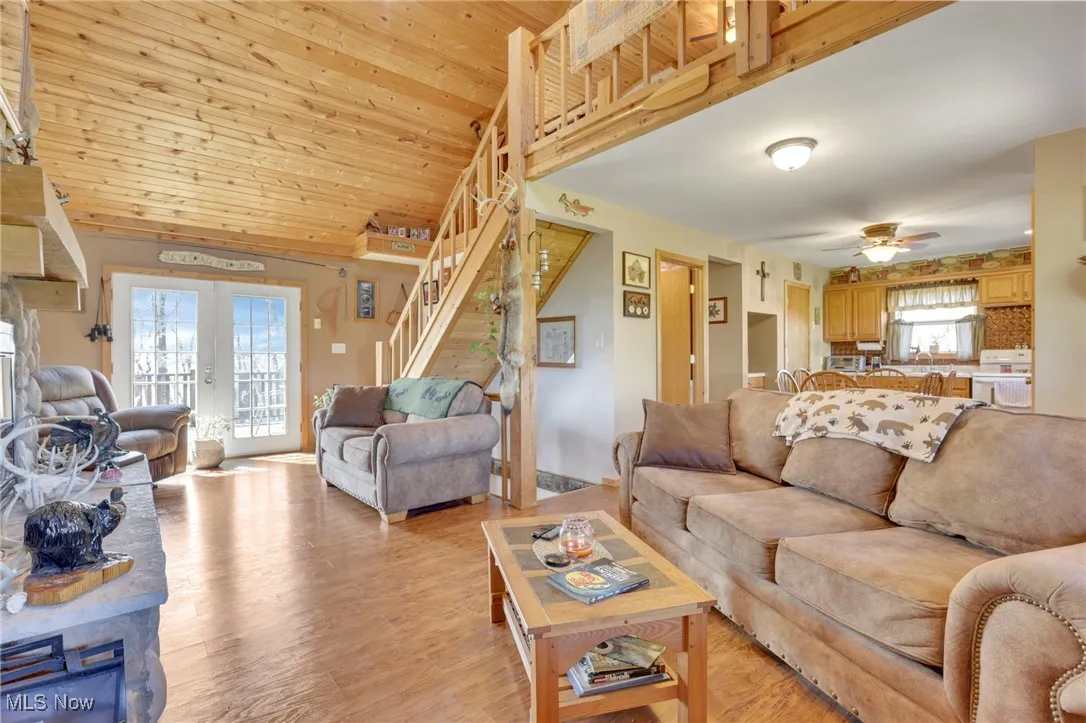 Living area featuring stairs, light wood-type flooring, ceiling fan, a fireplace, and lofted ceiling