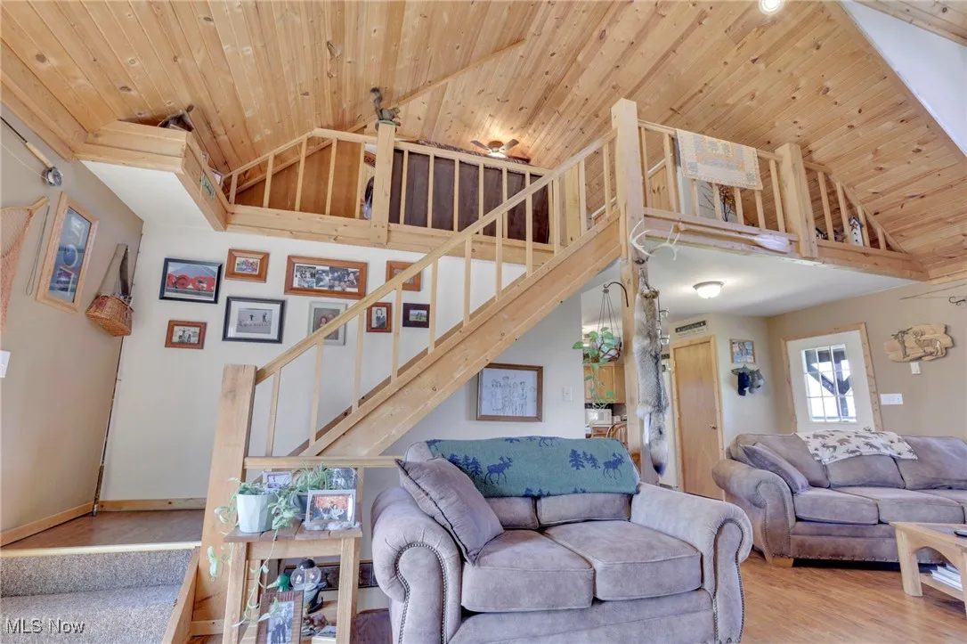 Living area with wooden ceiling, stairs, high vaulted ceiling, and wood finished floors