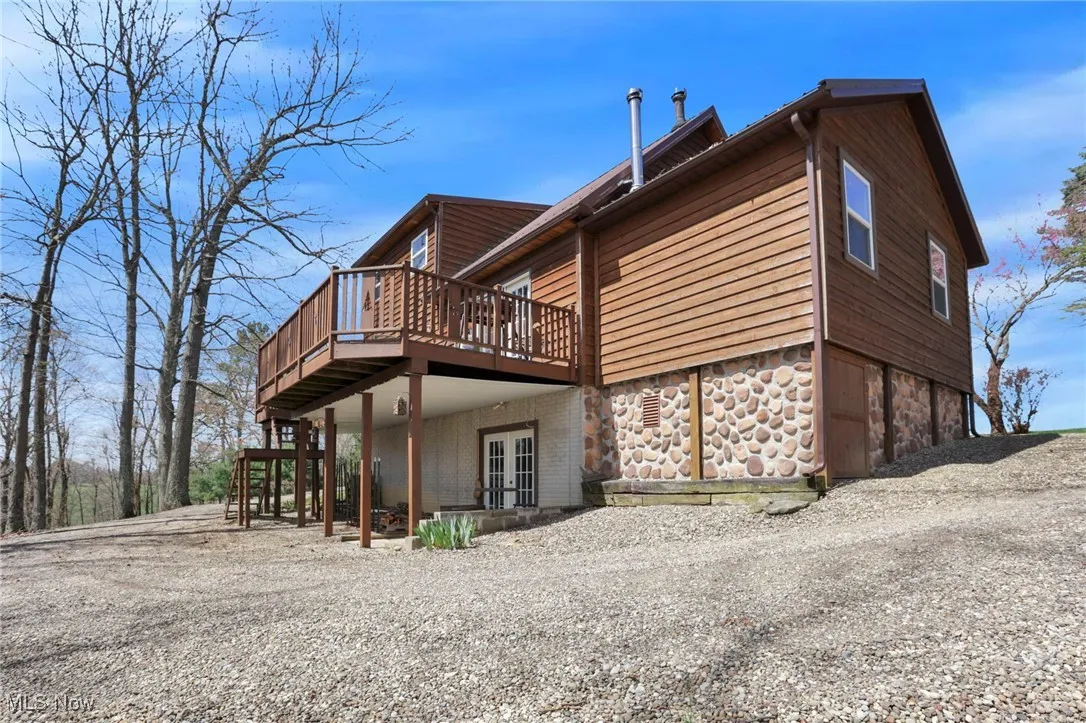 Rear view of house with a deck, gravel driveway, and stone siding