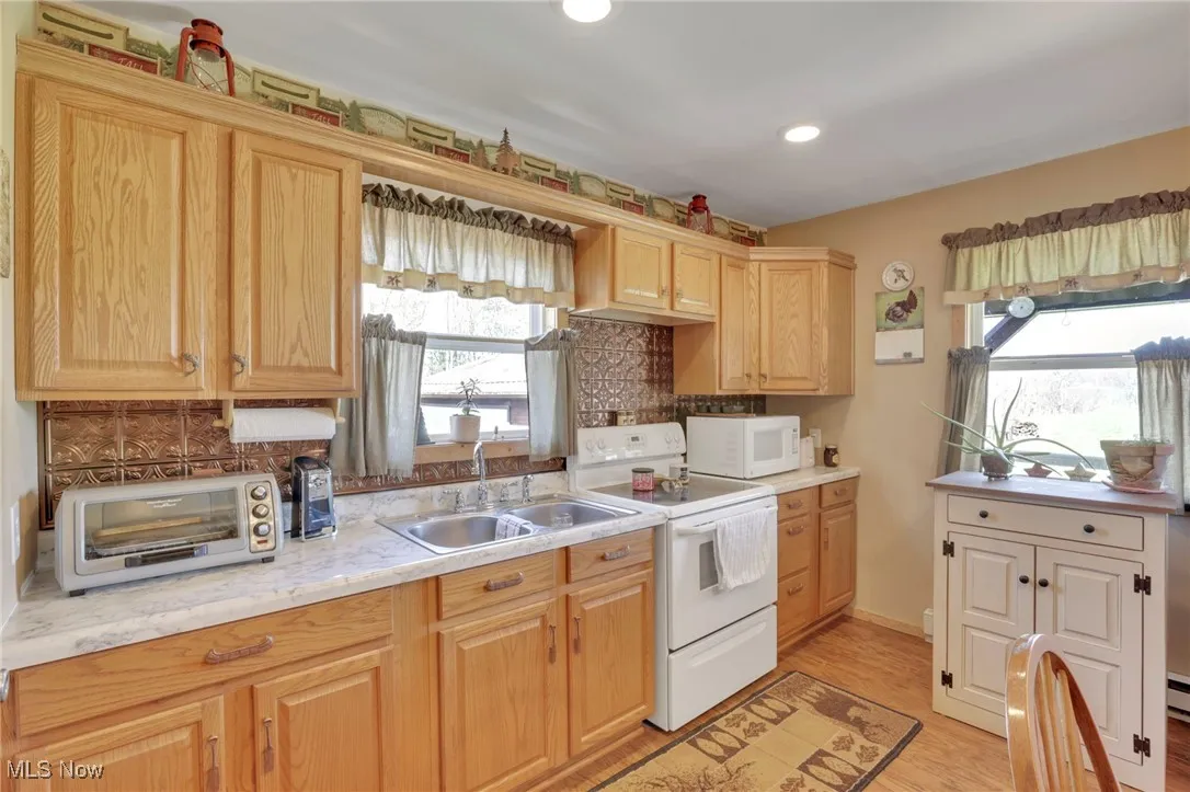Kitchen with white appliances, backsplash, light countertops, light wood-type flooring, and recessed lighting