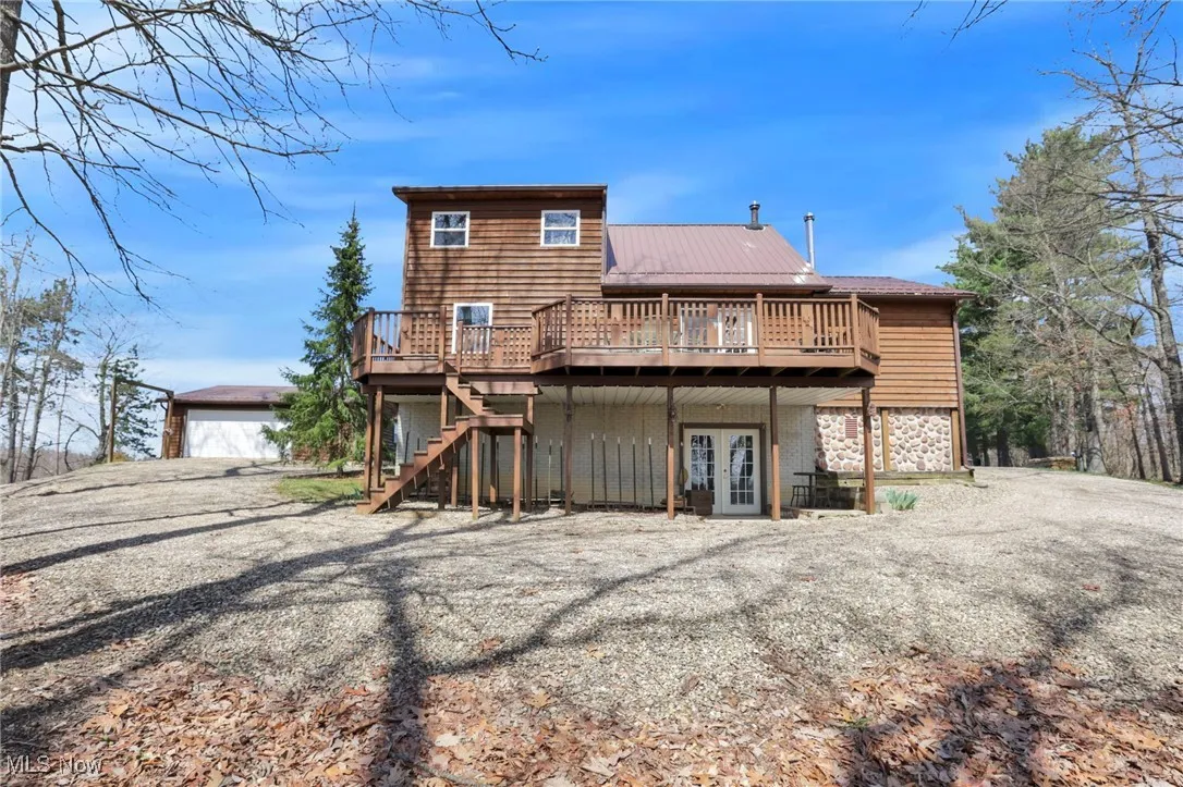Rear view of house with french doors, a deck, stone siding, stairway, and an outdoor structure