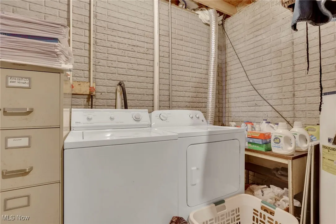 Laundry area with washer and clothes dryer, brick wall, and water heater
