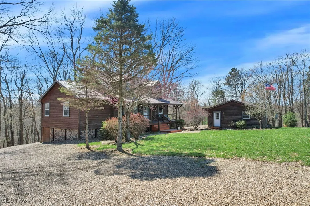 View of front of house with a carport, a porch, driveway, a front yard, and an outbuilding