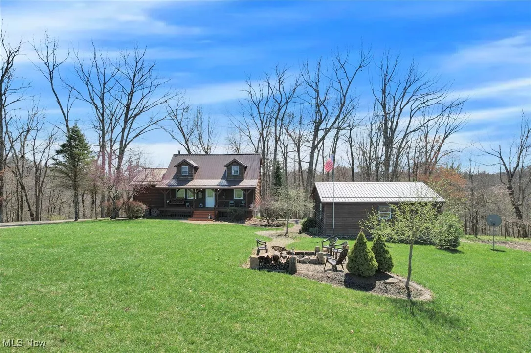 View of grassy yard featuring an outbuilding, a porch, and a fire pit