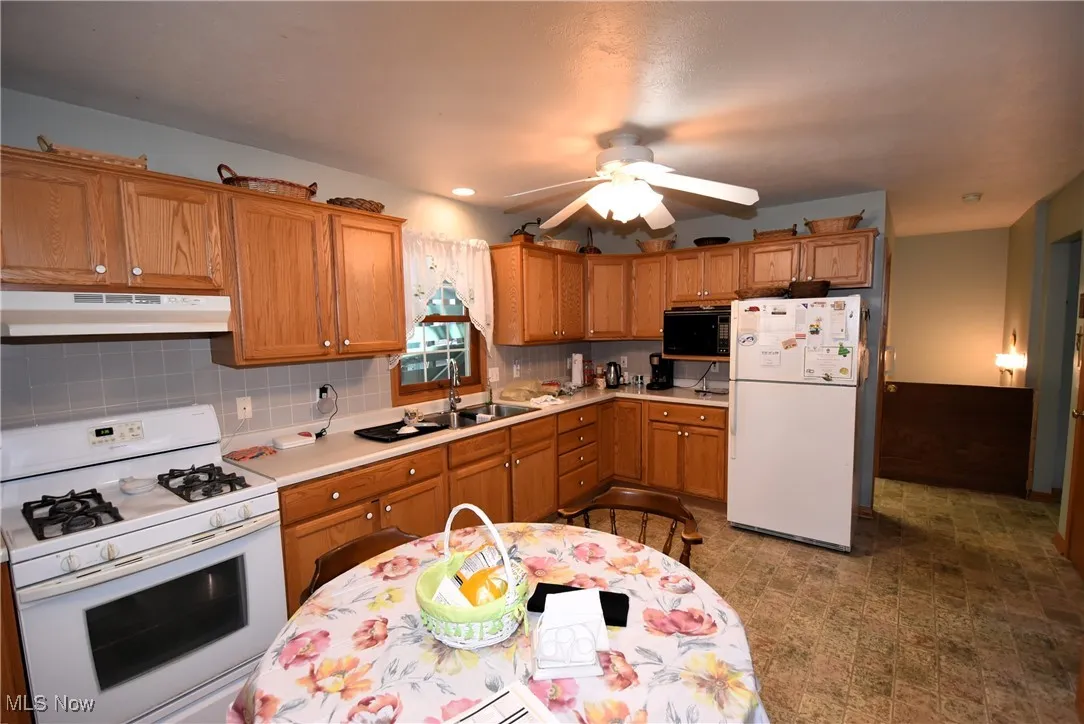 Kitchen featuring white appliances, under cabinet range hood, light countertops, ceiling fan, and tasteful backsplash