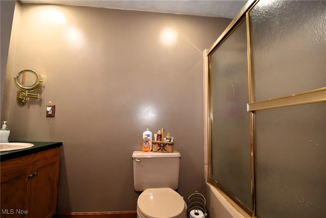Bathroom with vanity, enclosed tub / shower combo, and a textured ceiling
