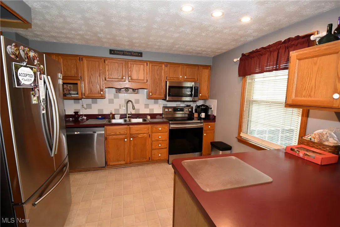 Kitchen featuring stainless steel appliances, a textured ceiling, backsplash, brown cabinets, and recessed lighting