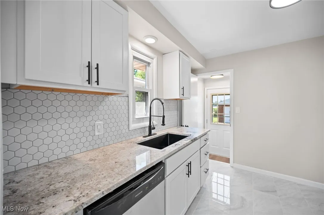 Kitchen featuring plenty of natural light, dishwasher, light stone counters, and white cabinets