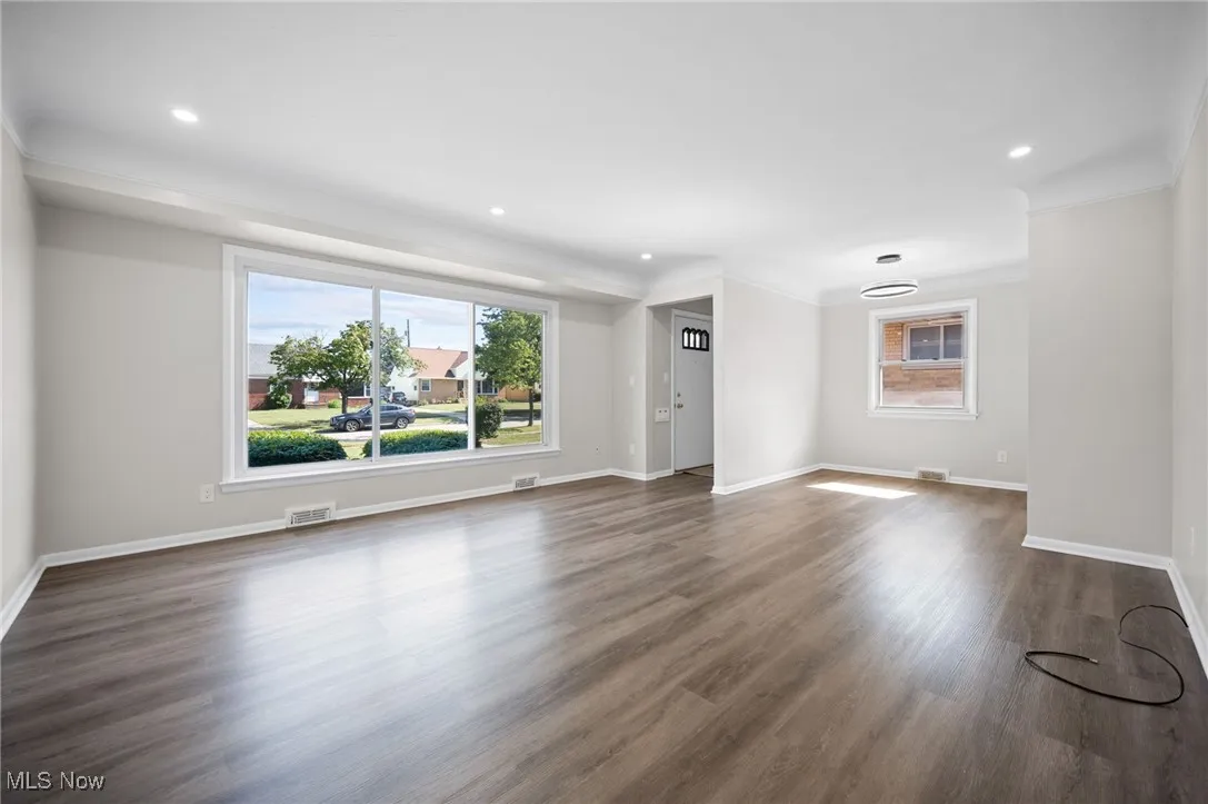 Unfurnished living room with plenty of natural light, dark wood finished floors, crown molding, and recessed lighting