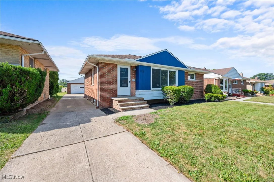 View of front of property featuring an outdoor structure, brick siding, a front yard, and a detached garage