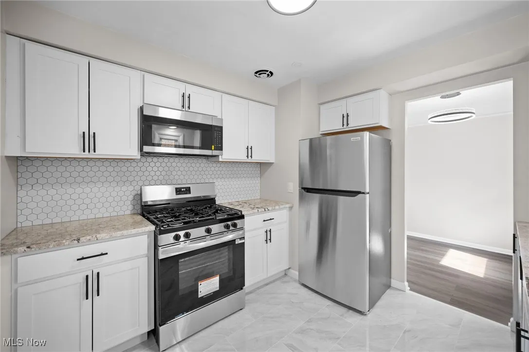 Kitchen featuring stainless steel appliances, white cabinetry, decorative backsplash, light stone countertops, and light marble finish floors