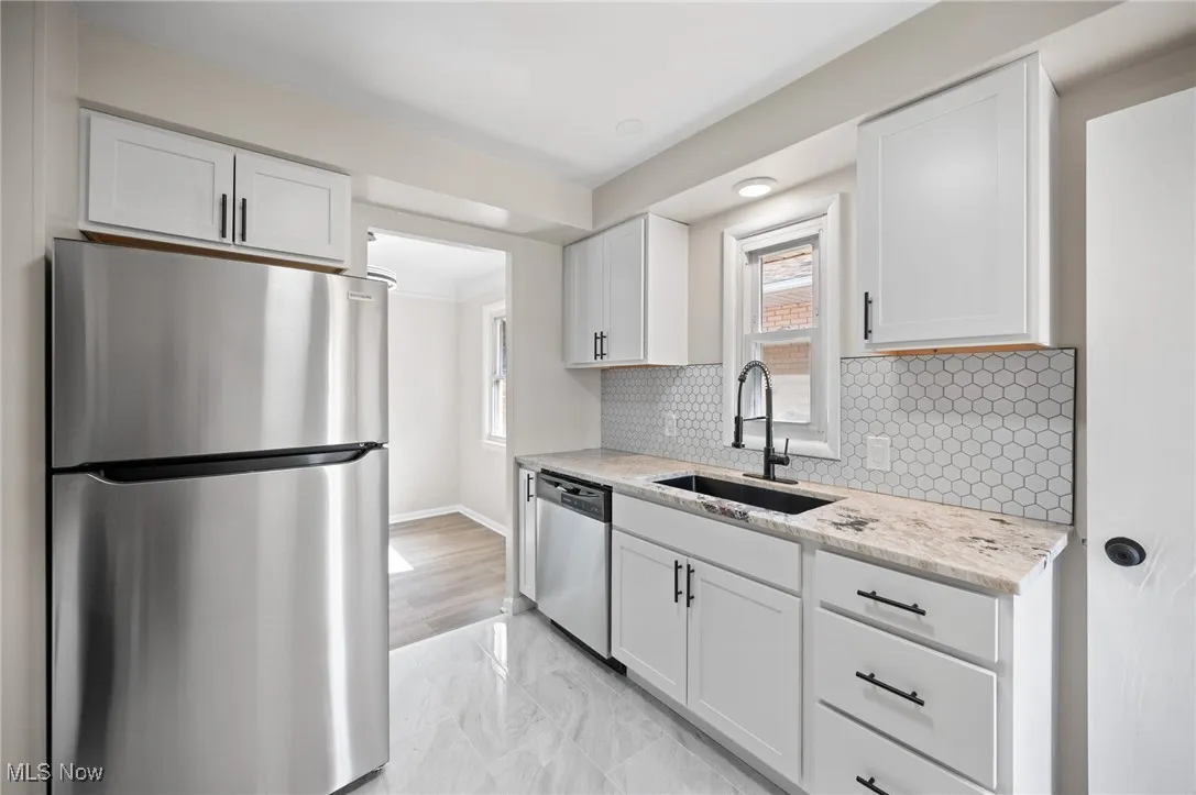 Kitchen with appliances with stainless steel finishes, decorative backsplash, white cabinetry, light stone counters, and light marble finish floors