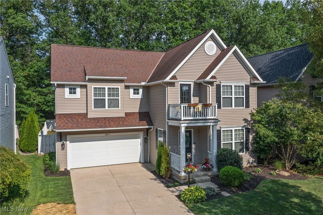 Traditional-style house featuring an attached garage, driveway, a balcony, and roof with shingles
