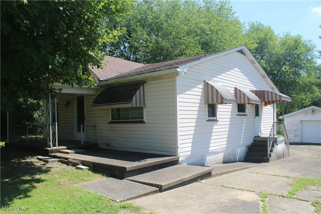 View of front of property featuring a shingled roof, an outdoor structure, a garage, and driveway