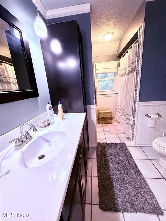 Bathroom with a wainscoted wall, vanity, a textured ceiling, tile patterned flooring, and curtained shower