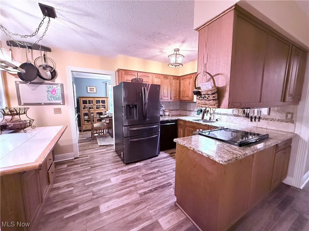 Kitchen featuring stainless steel fridge with ice dispenser, a peninsula, backsplash, wood finished floors, and dishwasher
