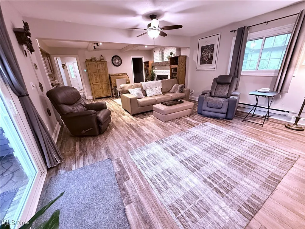 Living room with a ceiling fan, wood finished floors, a baseboard radiator, and a fireplace