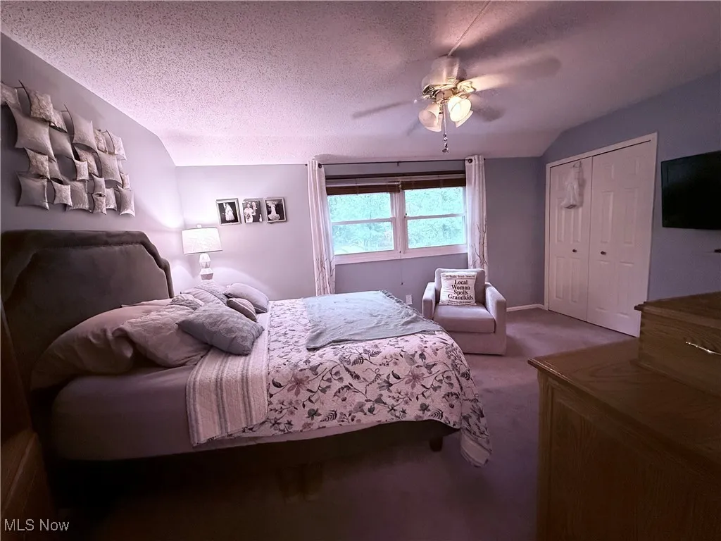 Bedroom with a textured ceiling, carpet, lofted ceiling, a ceiling fan, and a closet