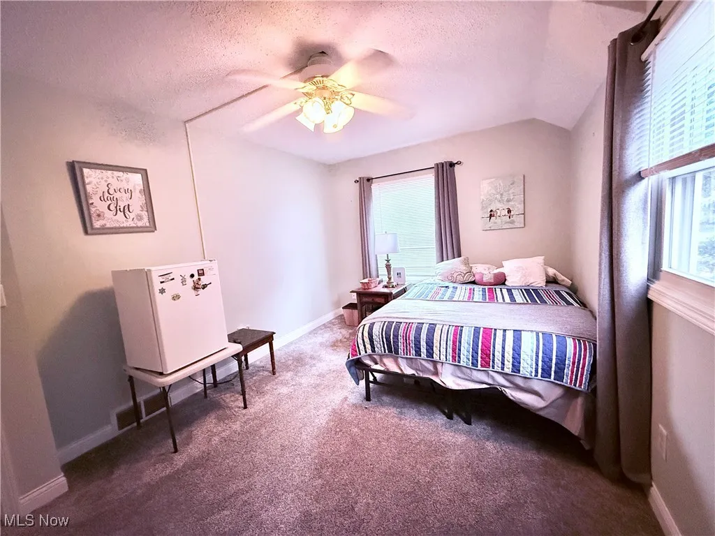 Carpeted bedroom with vaulted ceiling, a textured ceiling, and a ceiling fan