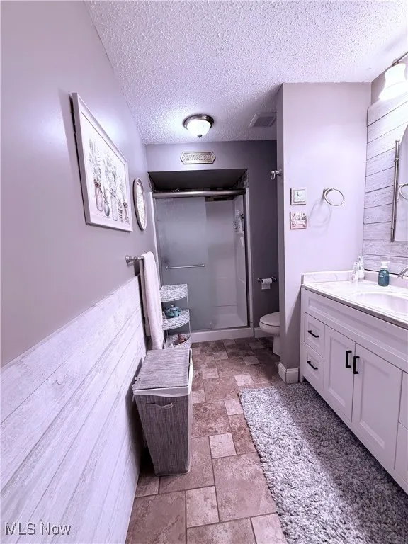 Full bathroom featuring vanity, a textured ceiling, a shower stall, and stone finish flooring