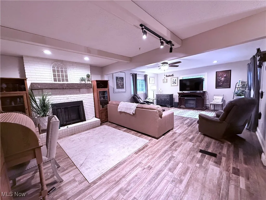 Living area with a brick fireplace, beam ceiling, recessed lighting, wood finished floors, and track lighting