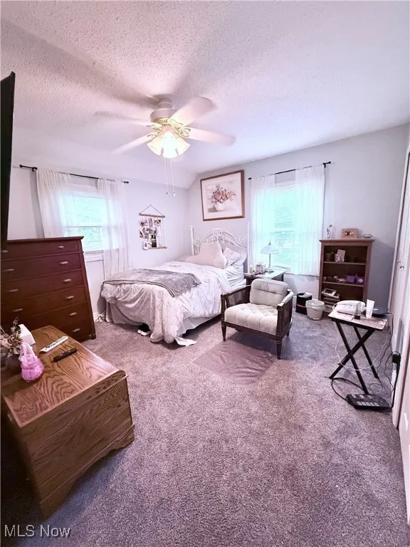 Bedroom with a textured ceiling, carpet, and ceiling fan
