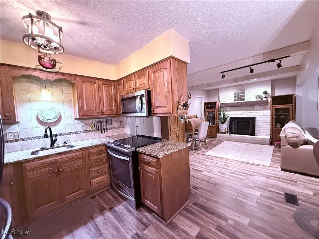 Kitchen with rail lighting, appliances with stainless steel finishes, dark wood-type flooring, a textured ceiling, and light stone countertops
