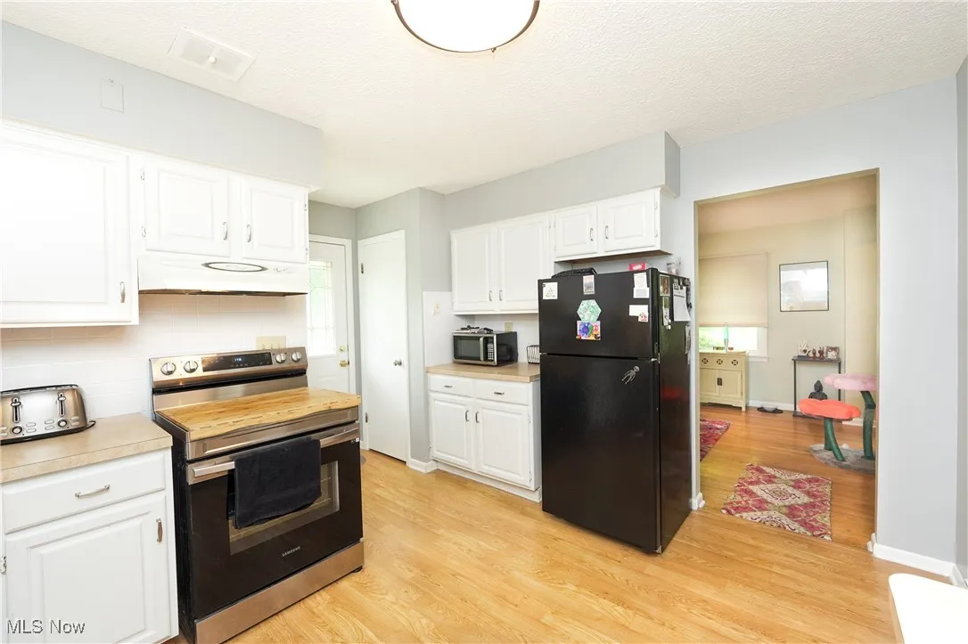 Kitchen with appliances with stainless steel finishes, light countertops, a textured ceiling, light wood-style floors, and under cabinet range hood