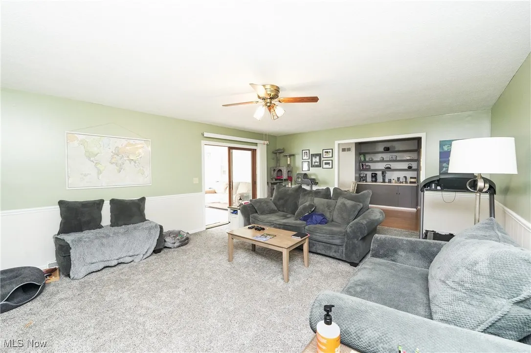 Living area featuring a wainscoted wall, ceiling fan, and carpet floors