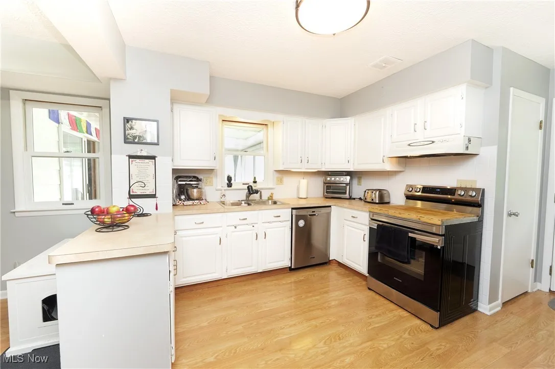 Kitchen with stainless steel appliances, light wood finished floors, light countertops, white cabinetry, and under cabinet range hood