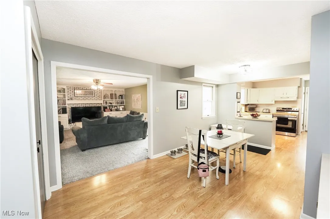 Dining area featuring a ceiling fan, light wood-style flooring, a fireplace, a textured ceiling, and light carpet
