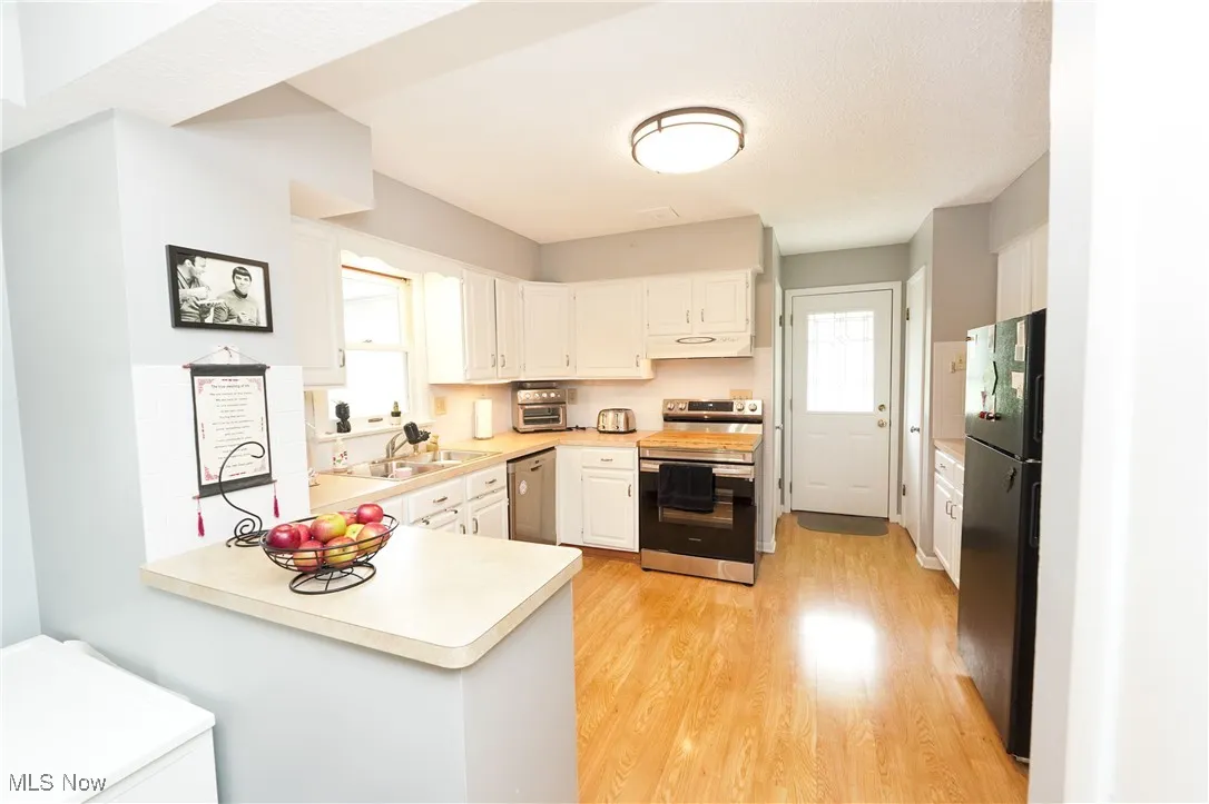 Kitchen featuring a peninsula, stainless steel appliances, light countertops, light wood-style floors, and white cabinets