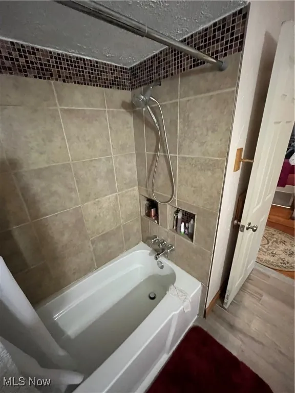 Bathroom with shower / bathtub combination, wood finished floors, and a textured ceiling