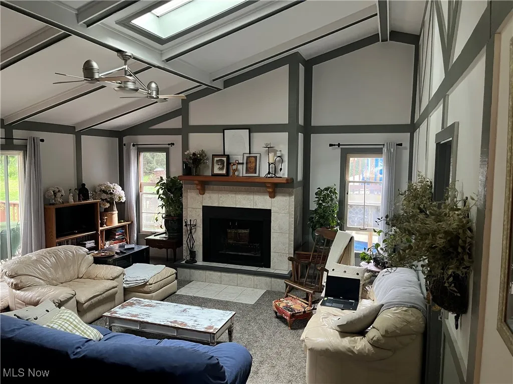 Living area with plenty of natural light, a tile fireplace, beamed ceiling, ceiling fan, and high vaulted ceiling