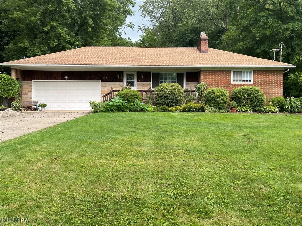 Single story home featuring a front yard, a chimney, driveway, a garage, and a shingled roof