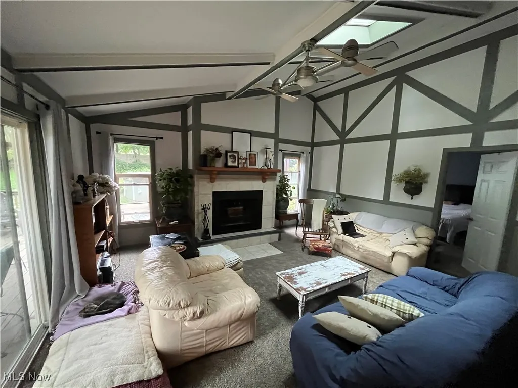 Living area featuring carpet flooring, a tile fireplace, beam ceiling, a ceiling fan, and high vaulted ceiling