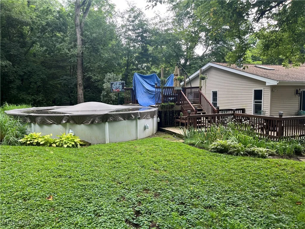 View of grassy yard featuring a deck and a covered pool