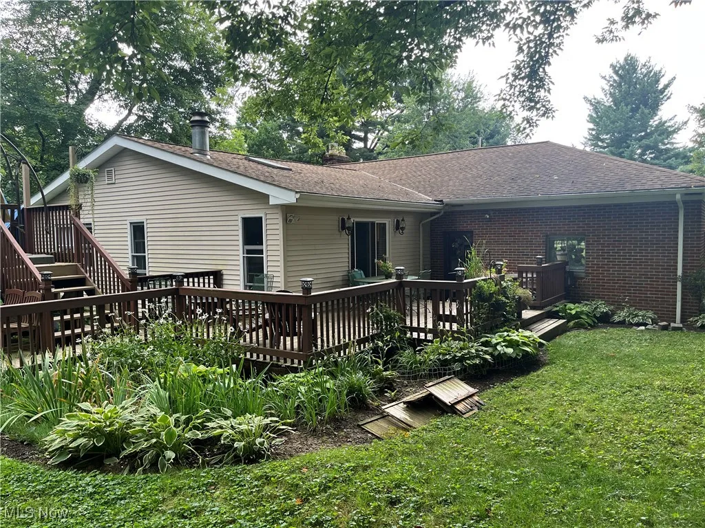 Back of house featuring a shingled roof, a deck, a lawn, and brick siding
