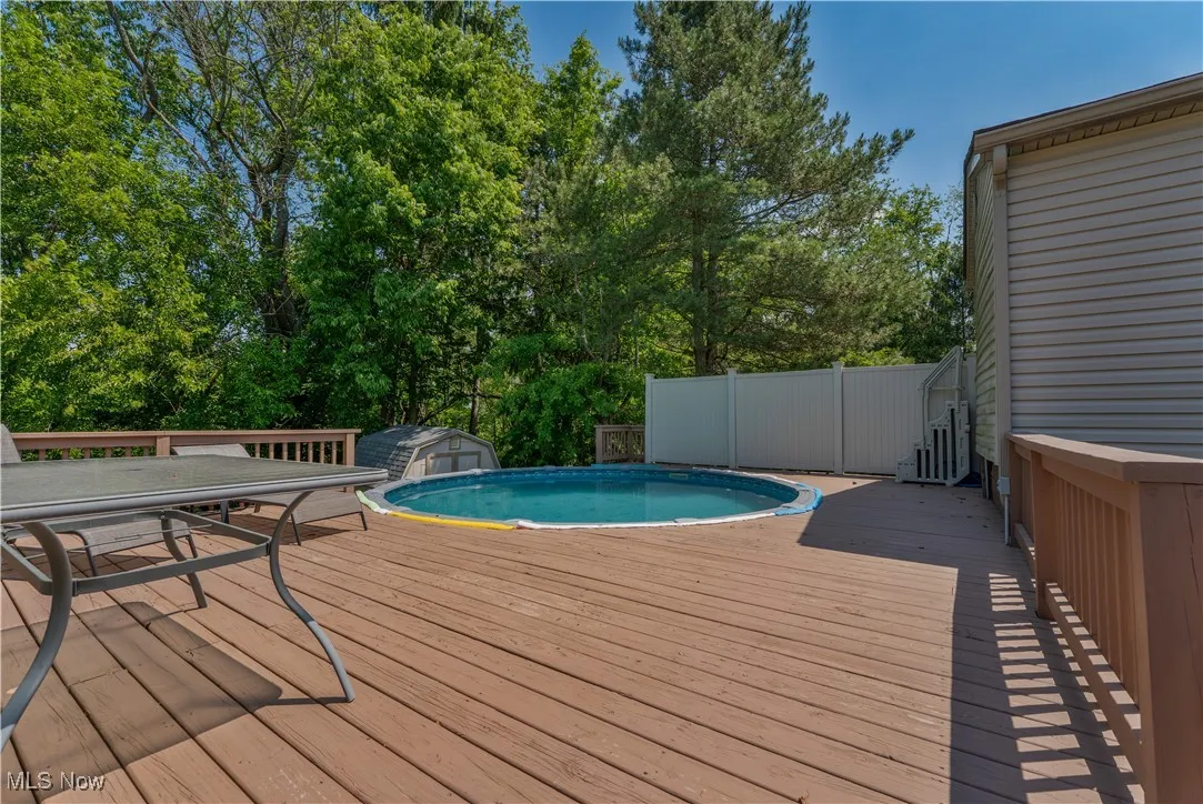 Wooden terrace with an outdoor pool, view of scattered trees, outdoor dining area, and a storage shed