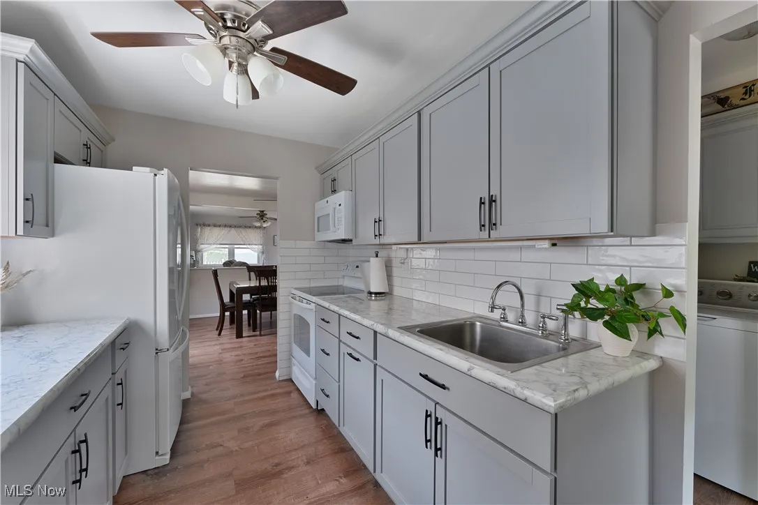 Kitchen featuring white appliances, a ceiling fan, washer / clothes dryer, and wood finished floors