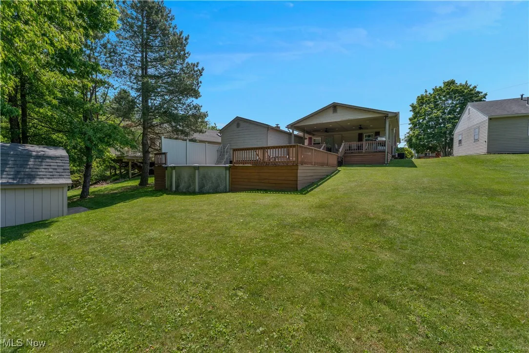 View of grassy yard with a wooden deck, a storage shed, and a swimming pool