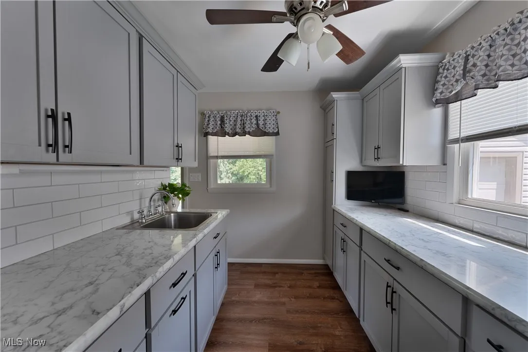 Kitchen featuring dark wood-type flooring, tasteful backsplash, light stone counters, a ceiling fan, and gray cabinets
