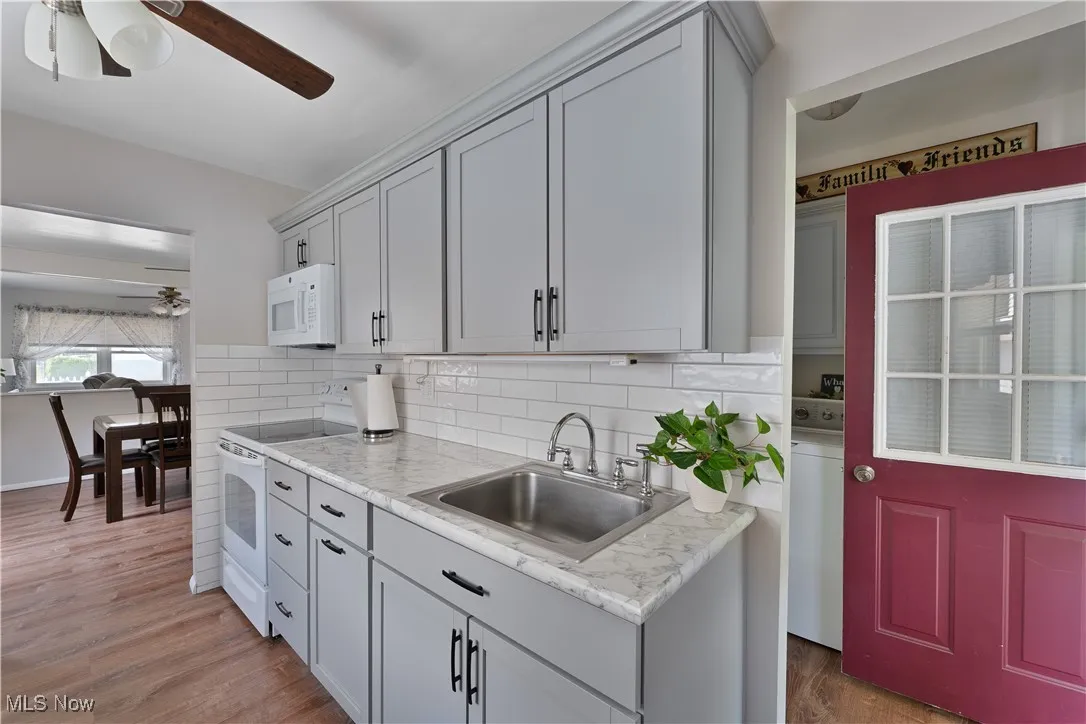 Kitchen featuring white appliances, ceiling fan, light wood-style flooring, and backsplash