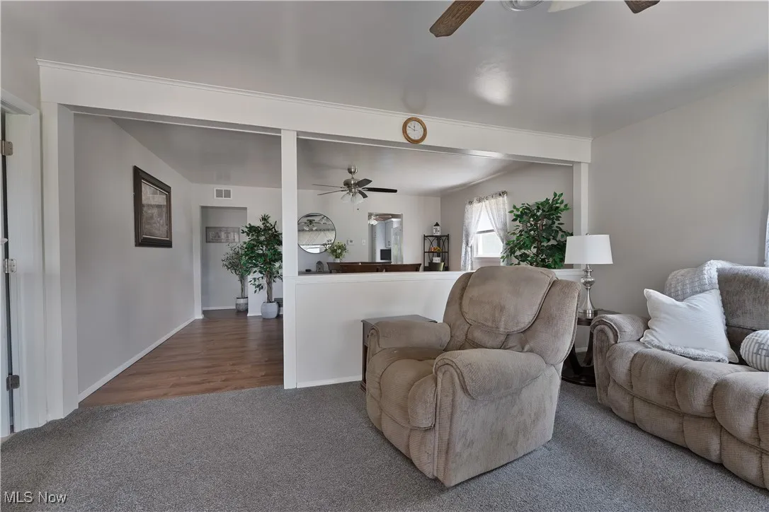 Carpeted living room featuring a ceiling fan and baseboards