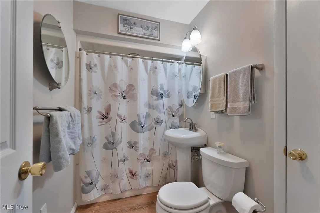 Bathroom with shower / bathtub combination with curtain and wood finished floors