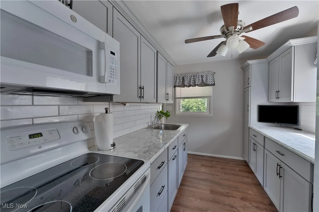 Kitchen featuring white appliances, decorative backsplash, dark wood-style floors, and light stone counters