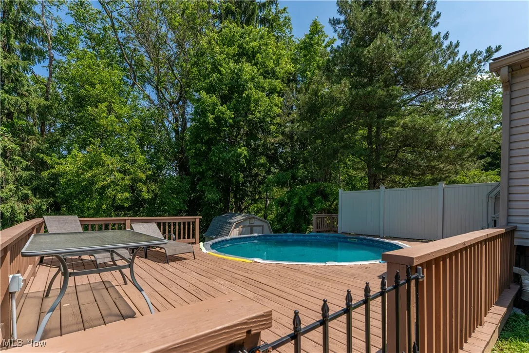 Swimming pool with a wooden deck, a storage shed, outdoor dining area, and view of scattered trees