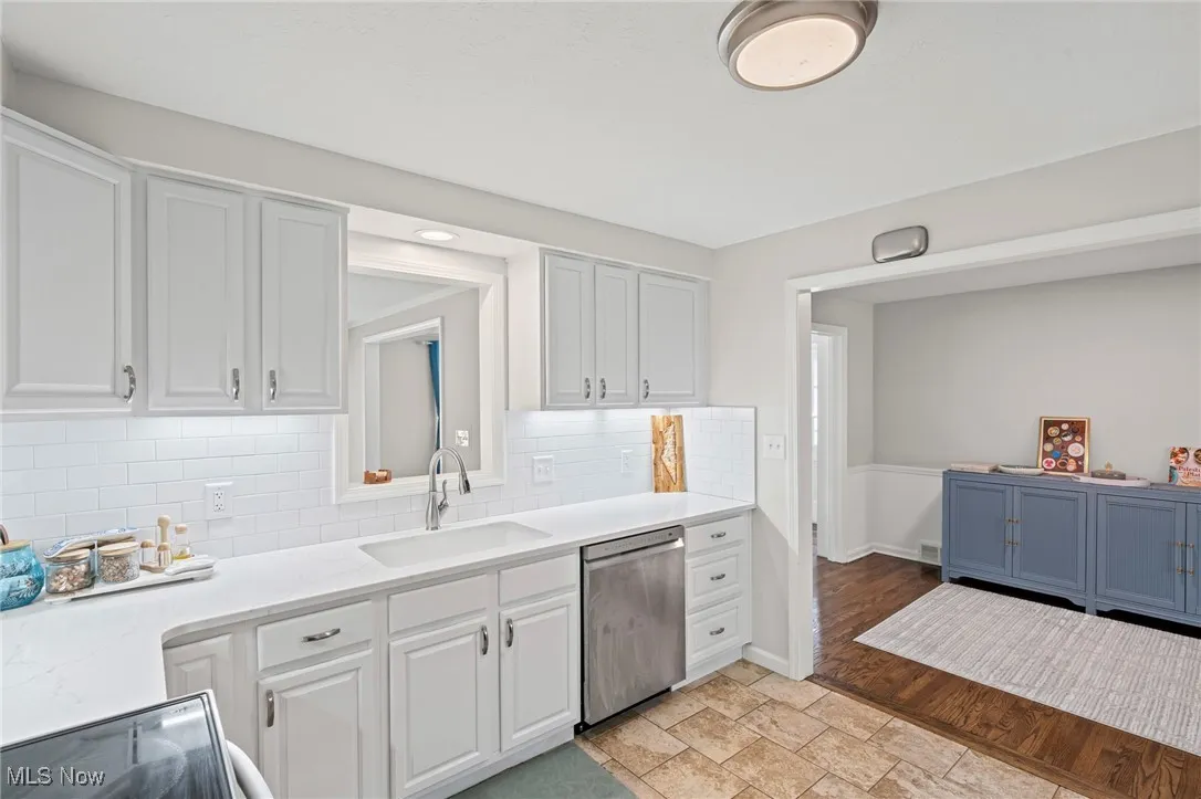 Kitchen featuring tasteful backsplash, light countertops, dishwasher, white cabinets, and stove