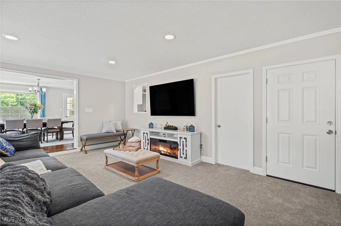 Carpeted living area with ornamental molding, a chandelier, recessed lighting, a glass covered fireplace, and a textured ceiling