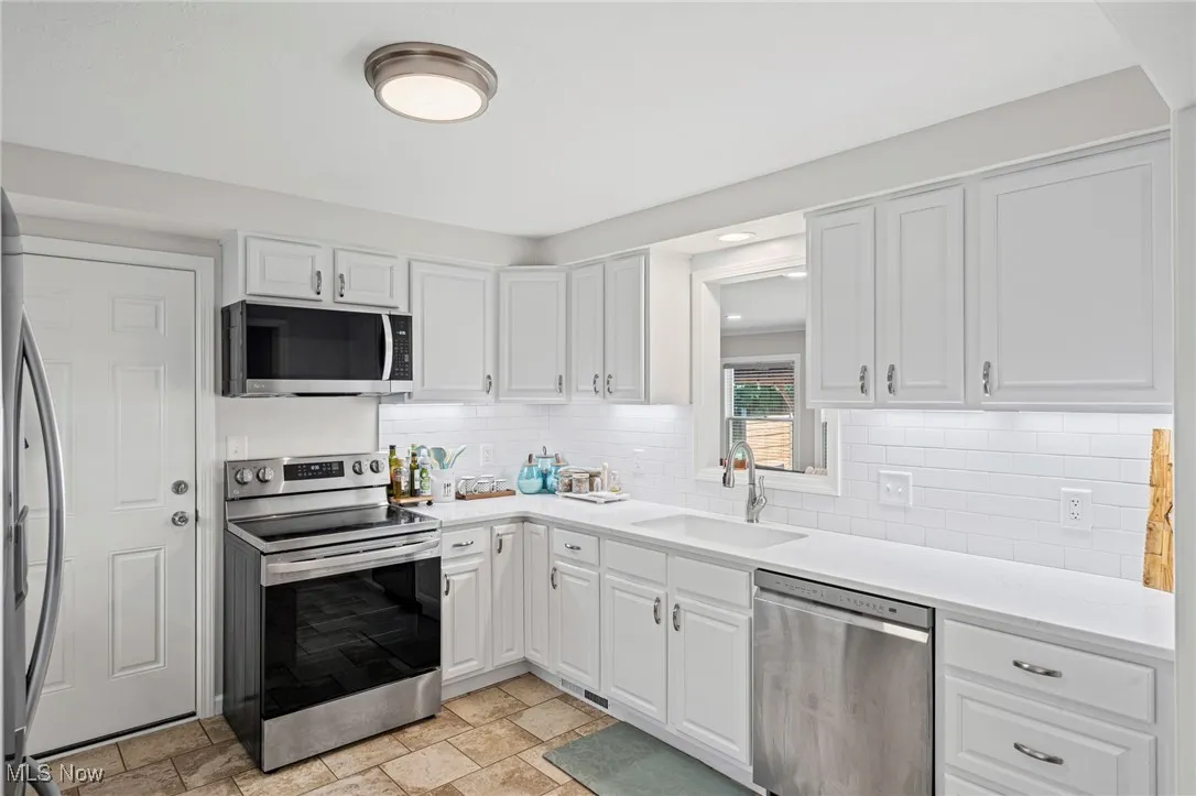 Kitchen with appliances with stainless steel finishes, white cabinets, backsplash, and light countertops